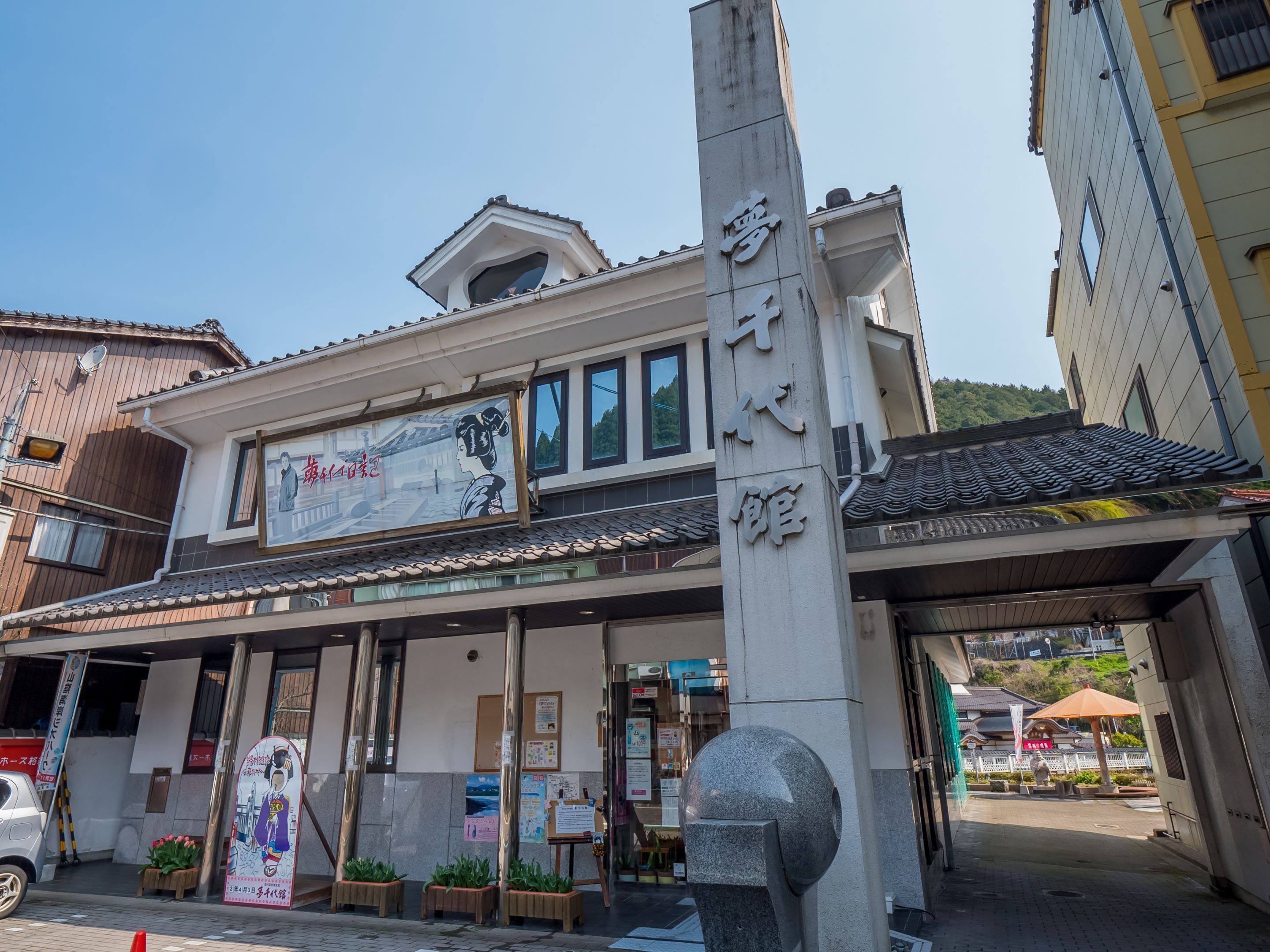 A traditional building with a large signboard, a stone pillar with inscriptions, and a tiled roof.