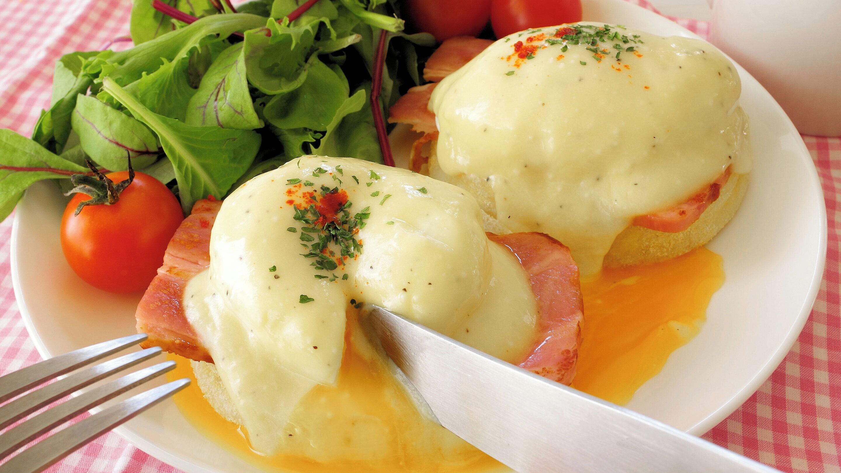 A plate with eggs benedict, a tomato, and a side salad.