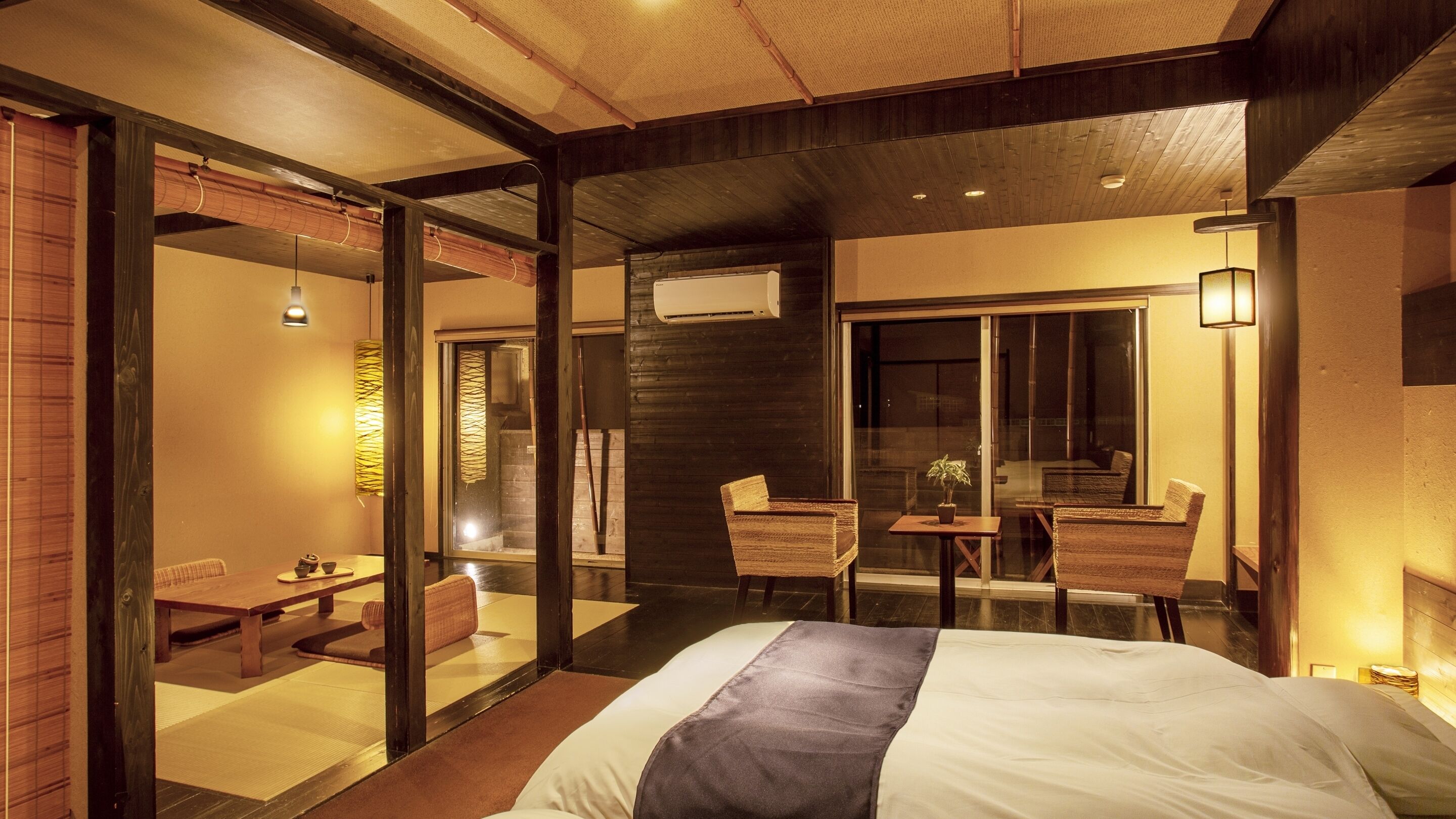 Een hotelkamer met een bed, een zithoek met een tafel en stoelen, een groot raam en een airconditioning.