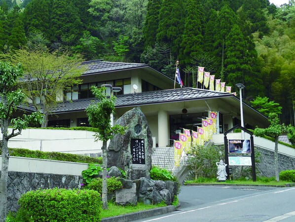 A traditional Japanese building with a stone entrance, surrounded by lush greenery and a stone wall. - Ooedo Onsen Monogatari Miyoshiya (Shinonsen)