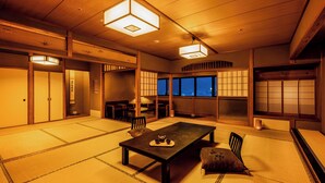 A traditional Japanese room with tatami flooring, a low table with a tea set, sliding doors, and large windows with night views. - Ooedo Onsen Monogatari Miyoshiya (Shinonsen)