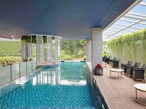 Piscina interior com piso ladrilhado, rodeada por um deck de madeira e mobiliada com assentos externos.
