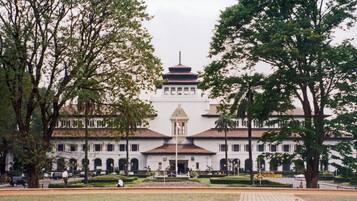 A large, historic building with a central dome and multiple wings, surrounded by well-maintained gardens and trees.