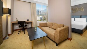 A hotel room with a bed, a sofa, a desk with a chair, a lamp, and a view of a cityscape. - Mercure Bandung Nexa Supratman (Bandung)