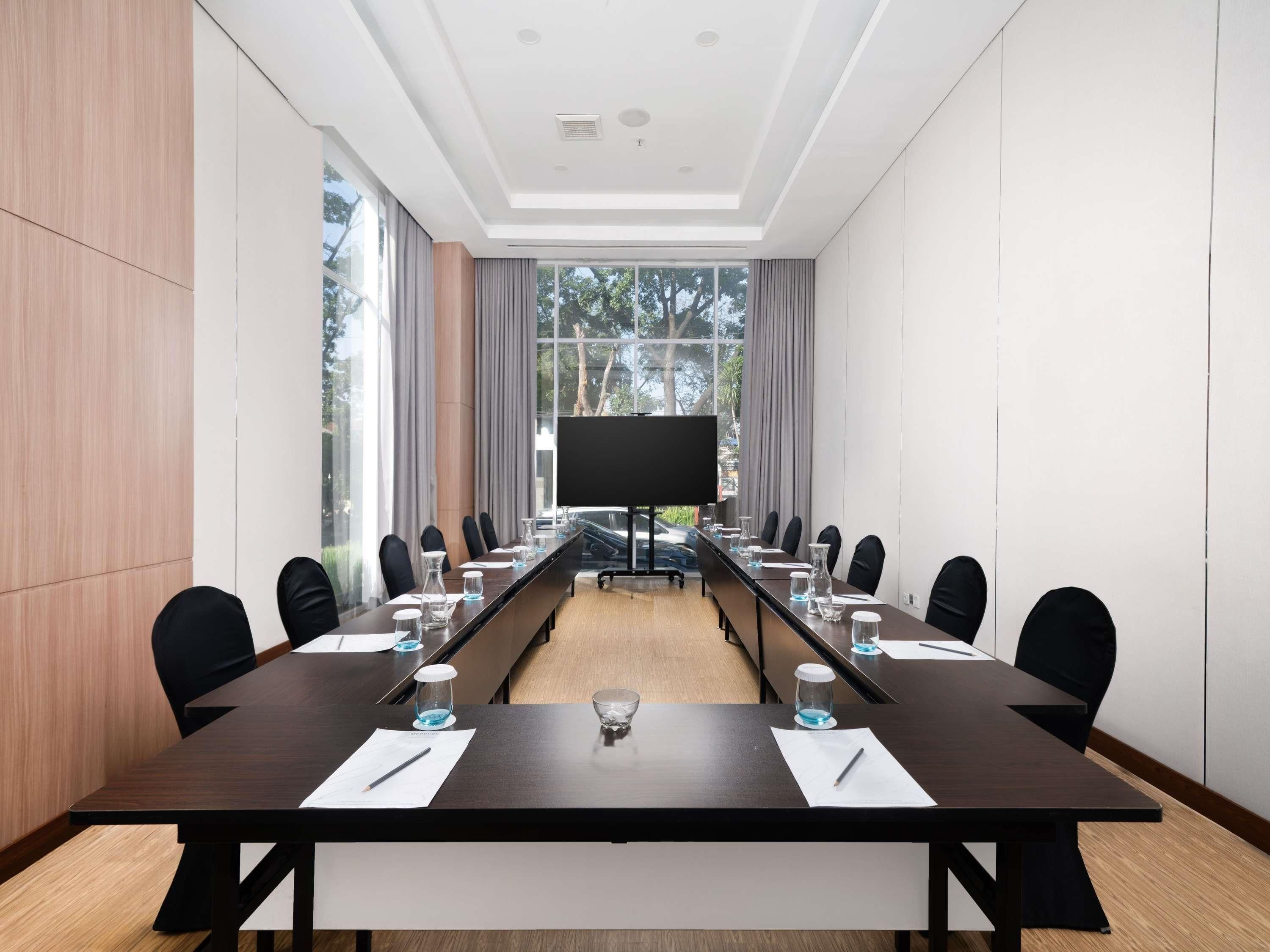 A conference room with a long table, chairs, a projector screen, and large windows.