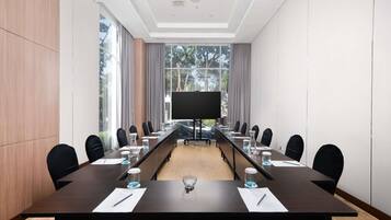 A conference room with a long table, chairs, a projector screen, and large windows.