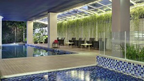 Ein Swimmingpool mit blauen Mosaikfliesen, umgeben von Liegestühlen und einem mit Glas bedeckten Bereich mit hängenden Pflanzen.