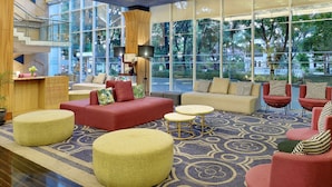 Eine großzügige Lobby mit modernem Design, mit verschiedenen Sitzbereichen, einem Empfangstresen und großen Fenstern mit Blick ins Freie.