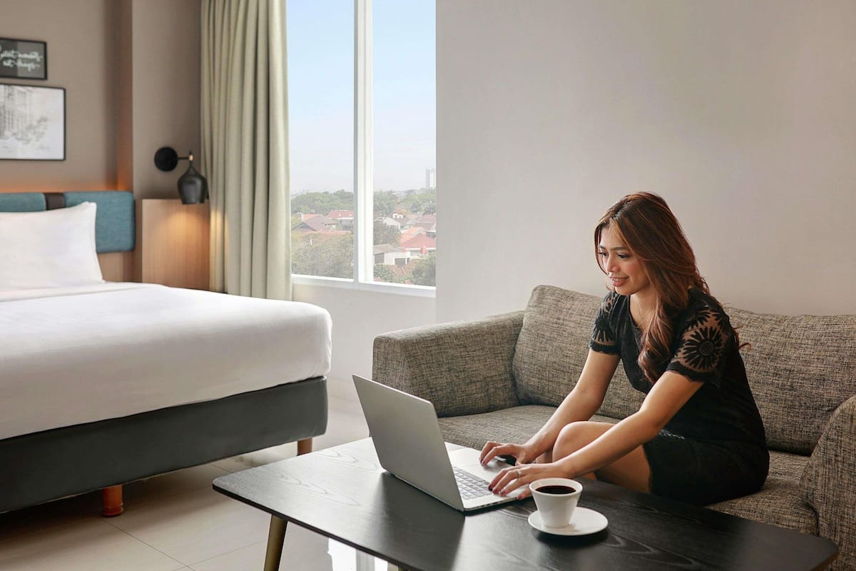 A hotel room with a bed, a sofa, a laptop, and a cup of coffee on a table.