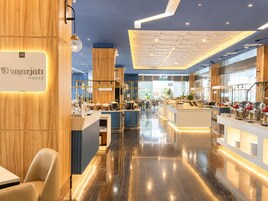 En modern hotellobby med en central receptionsdisk, ett matområde och ett kök som syns i bakgrunden.