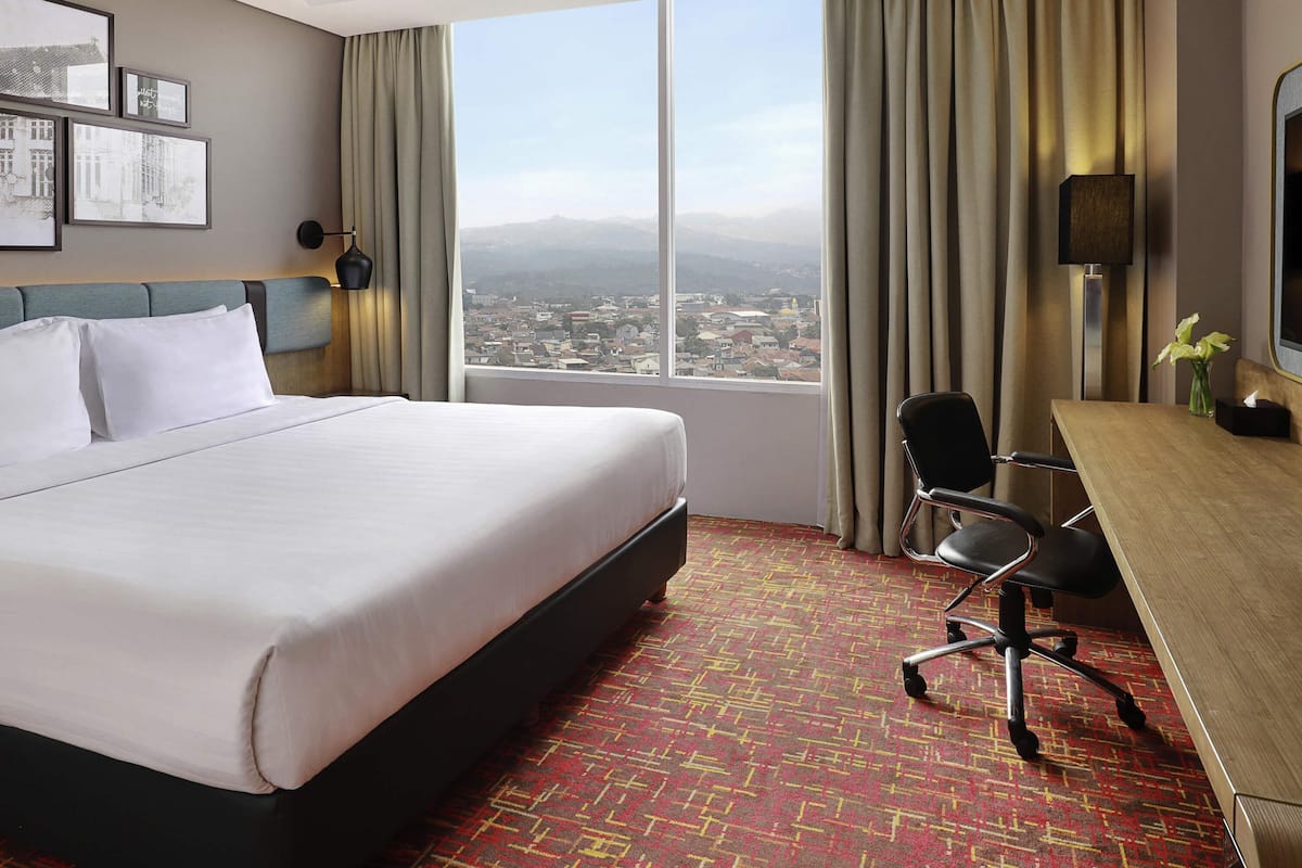 Une chambre d’hôtel avec un grand lit, un bureau avec une chaise, une télévision et une vue sur le paysage urbain.