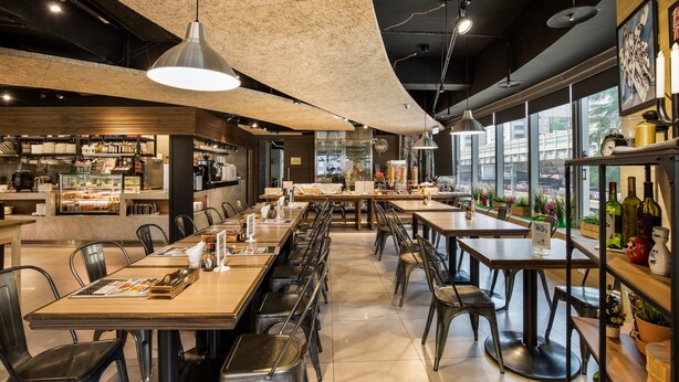 Un ristorante moderno con soffitti alti, travi a vista e ampie finestre. Tavoli e sedie disposti per la ristorazione.