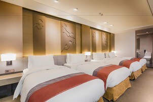 Une chambre d’hôtel avec quatre lits, chacun recouvert d’une courtepointe rouge et blanche, et un mur orné de panneaux décoratifs.