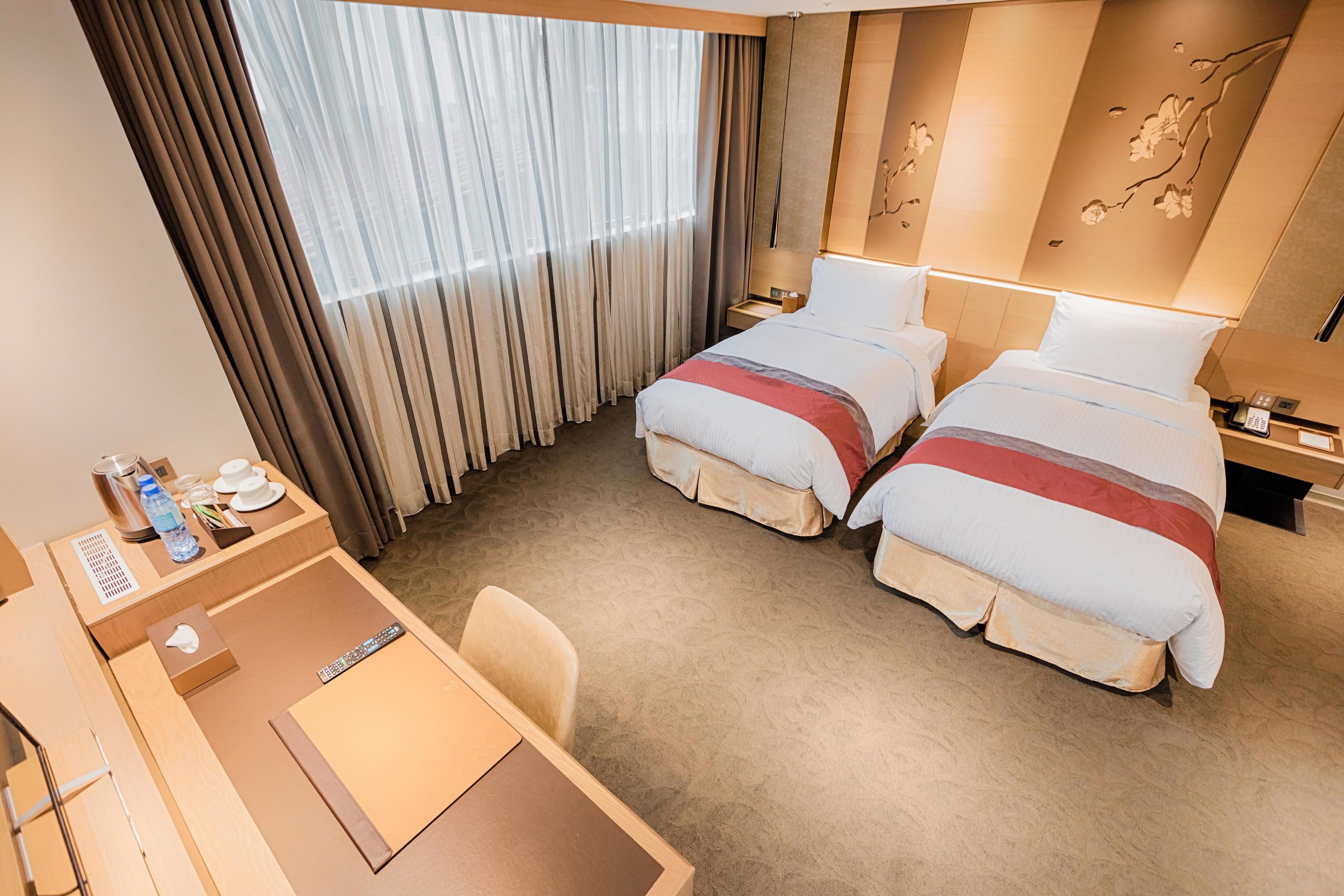 A hotel room with two beds, a desk, and a chair.