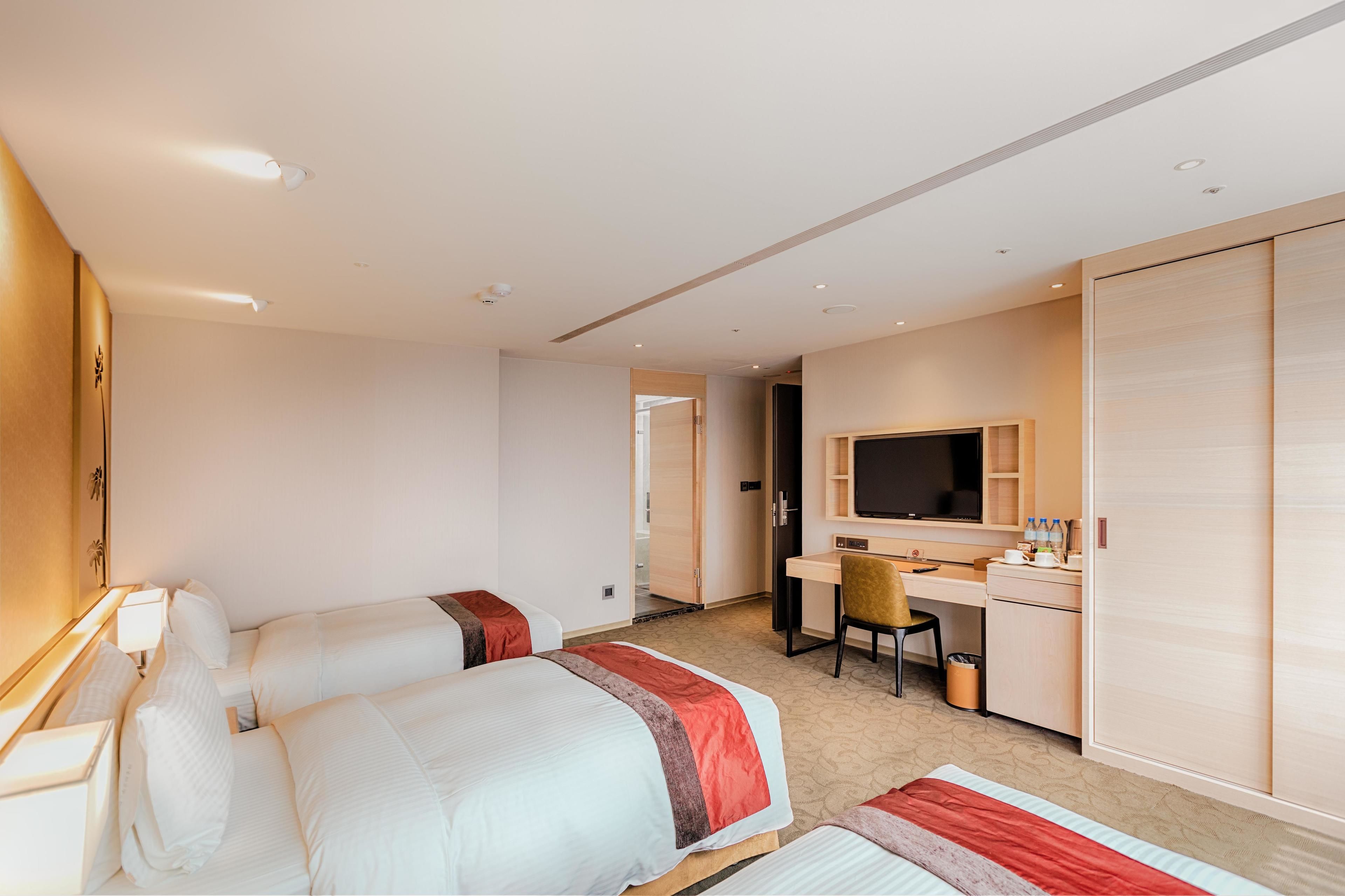 A hotel room with two beds, a desk, a chair, a television, and a wardrobe.