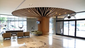Una hall dal design moderno, con una struttura centrale in legno, zona salotto con divani e un'ampia entrata in vetro.