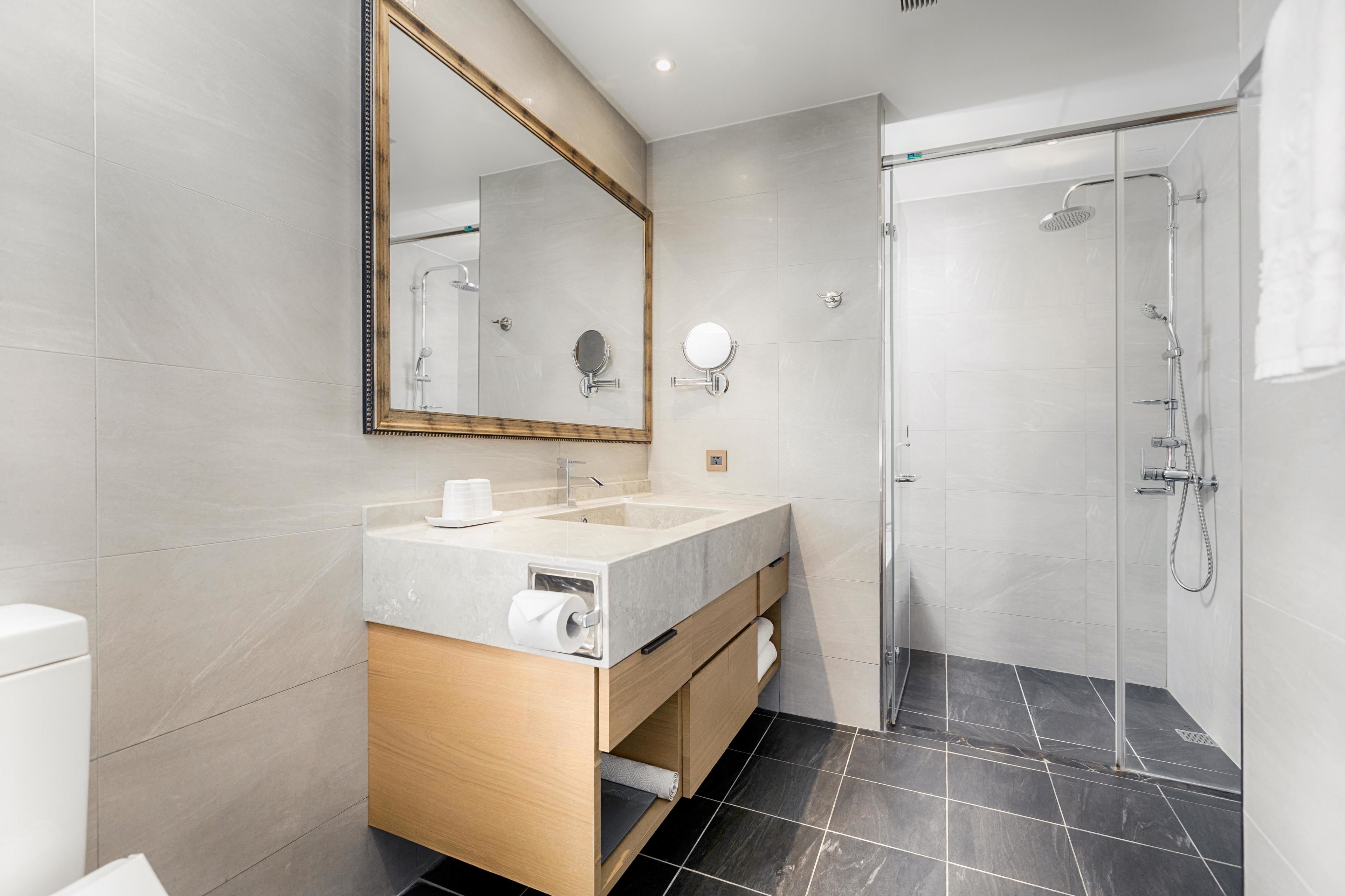 A modern bathroom with a double sink vanity, a large mirror, a shower with a glass door, and dark tiled flooring.