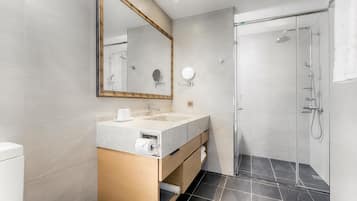 A modern bathroom with a double sink vanity, a large mirror, a shower with a glass door, and dark tiled flooring.