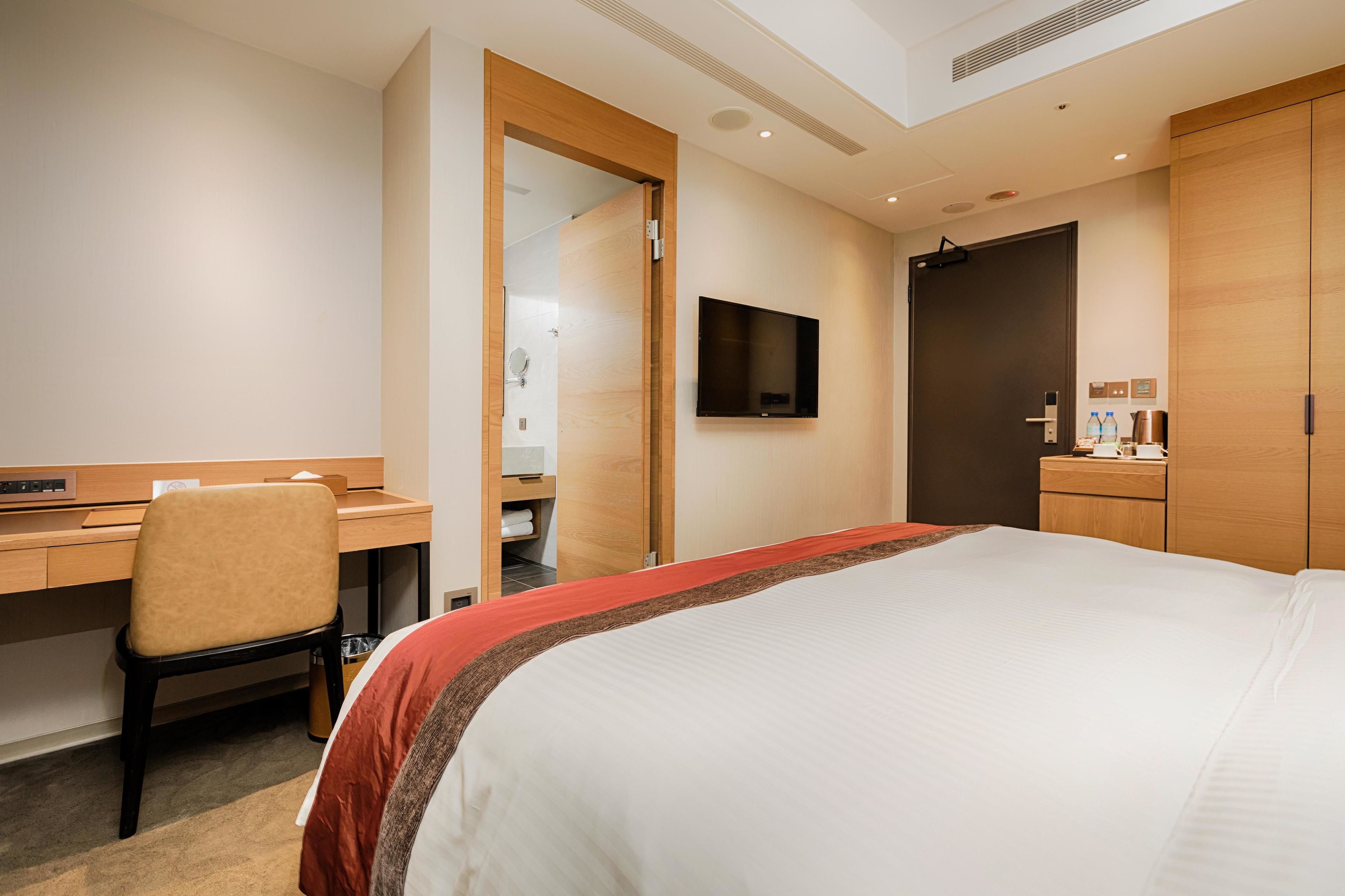 Une chambre d’hôtel équipée d’un lit, d’un bureau, d’une chaise, d’un téléviseur fixé au mur et d’une armoire.