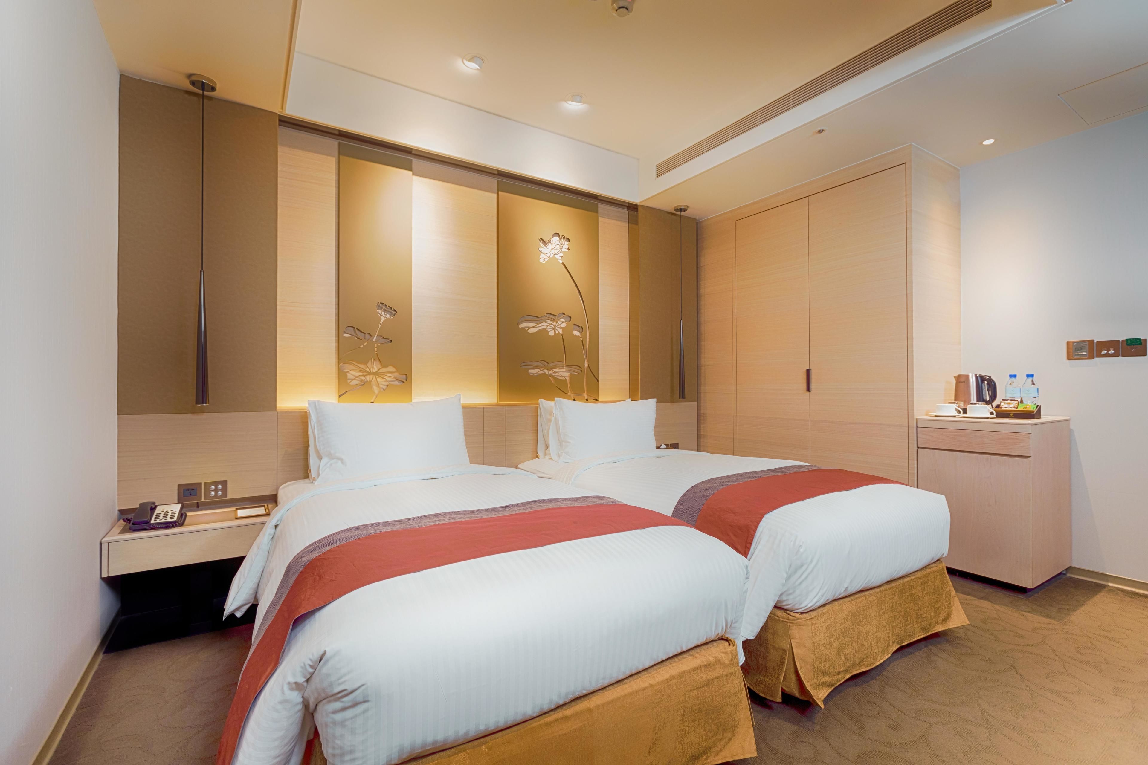 A hotel room with two beds, a nightstand, a desk, and a wardrobe.
