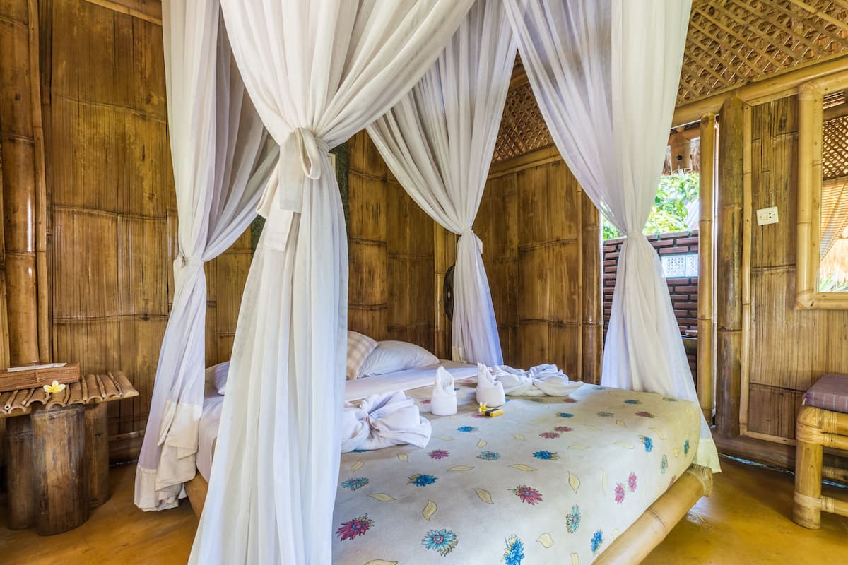 Un lit à baldaquin à quatre poteaux, agrémenté d’une couvre-lit à motifs floraux, avec des murs en bois et un petit tabouret en bois.