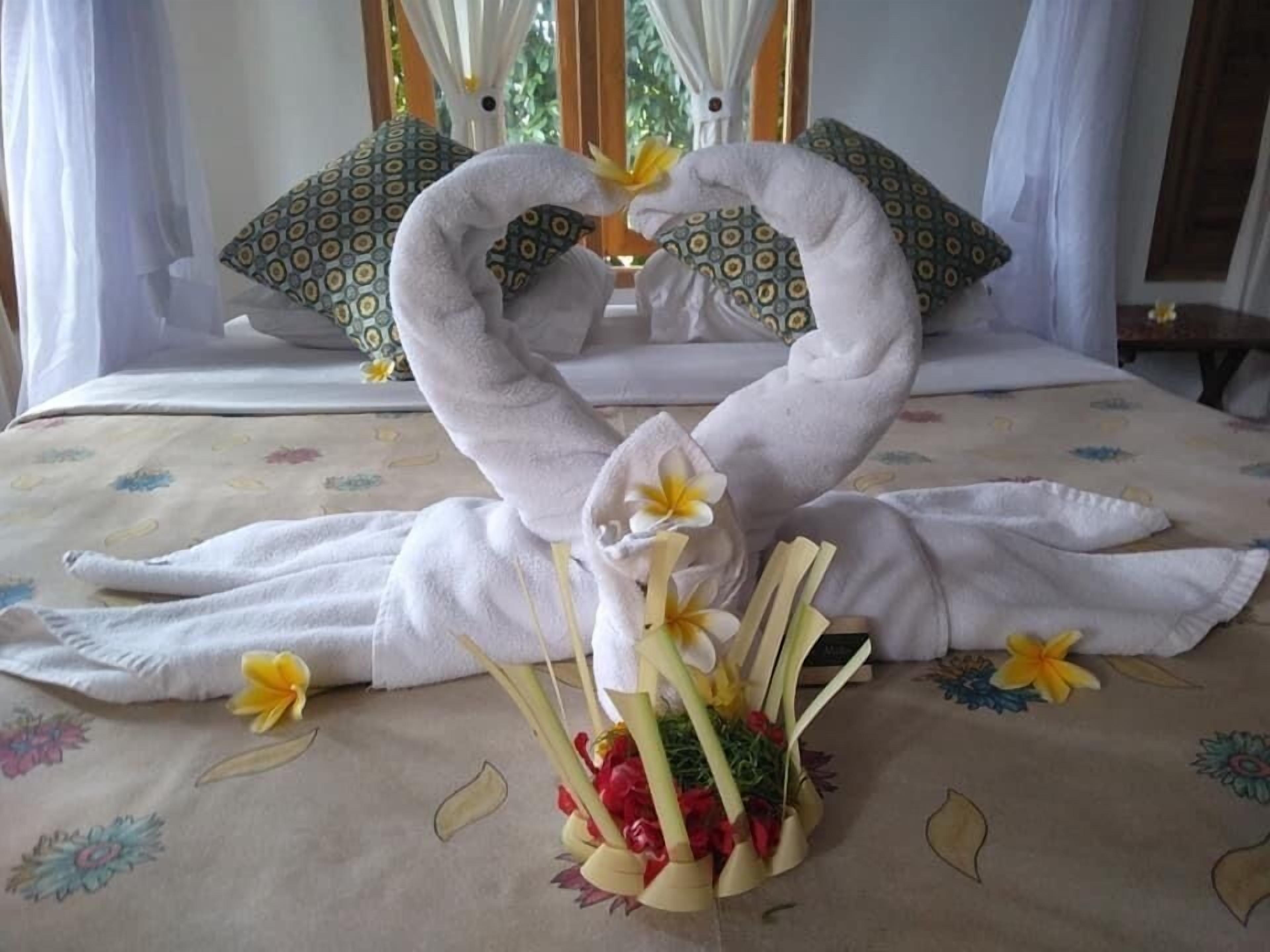 A bed with a towel swan centerpiece, pillows, and a floral arrangement.