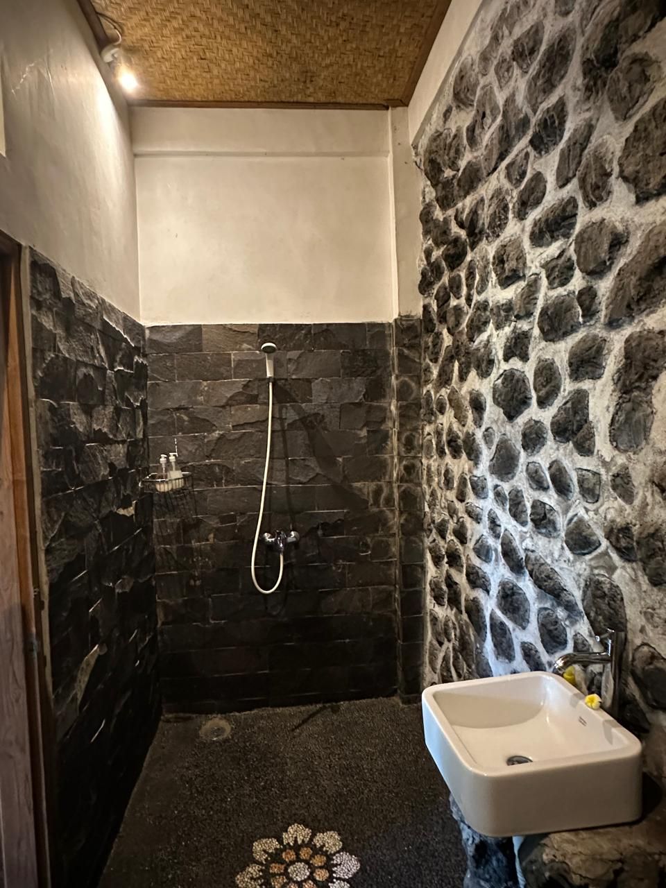 A bathroom with a stone wall, a shower, and a sink.