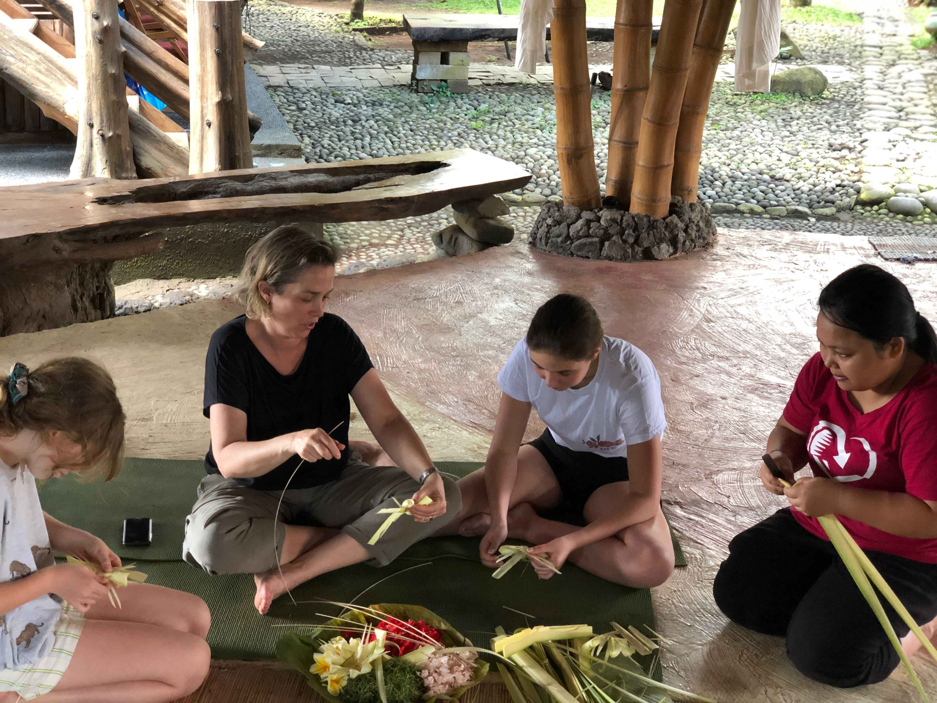 A group of people sitting on mats, engaged in an activity with bamboo sticks and flowers.