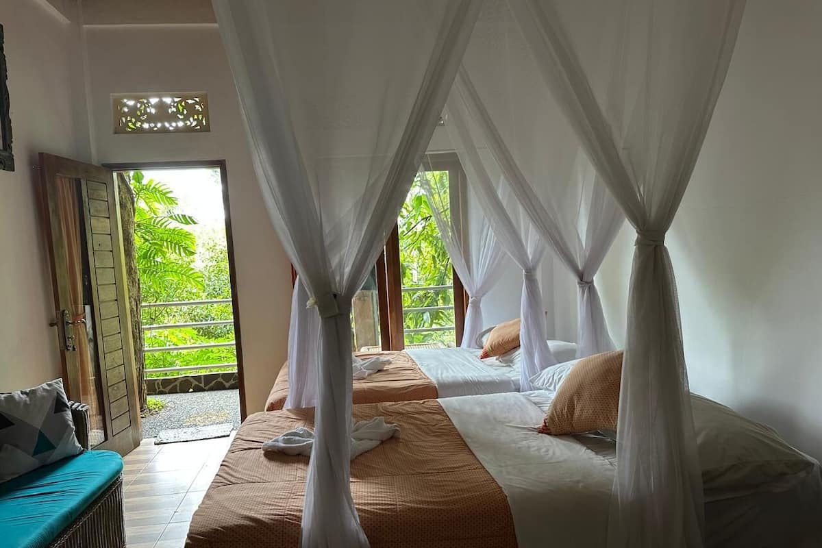 Une chambre avec deux lits, chacun recouvert d’un moustiquaire blanc, et une vue sur une végétation luxuriante.