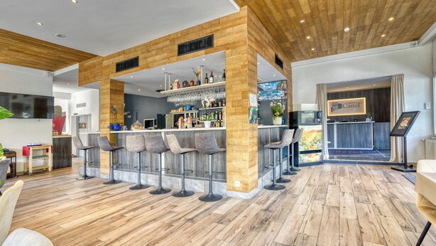 Un moderno vestíbulo de hotel con zona de bar, suelo de madera y taburetes contemporáneos.