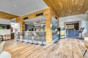 A modern hotel lobby with a bar area, wooden flooring, and contemporary bar stools. - Hotel Castel (Sion)