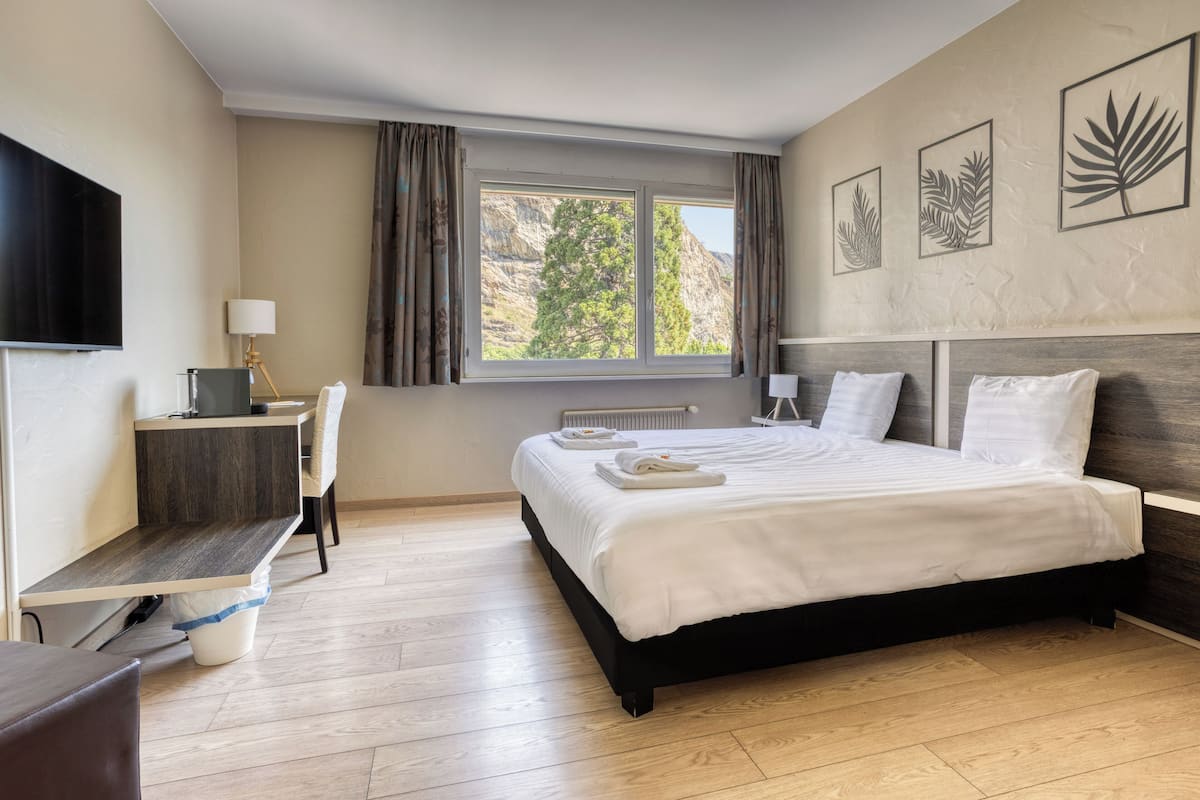 Habitación de hotel con cama, escritorio, silla, televisor y ventana con cortinas.