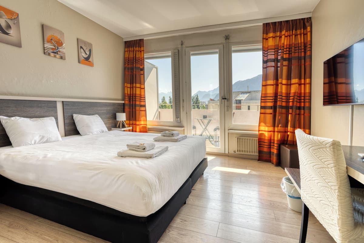 Habitación de hotel con una cama grande, un escritorio y vistas a montañas a través de las ventanas.