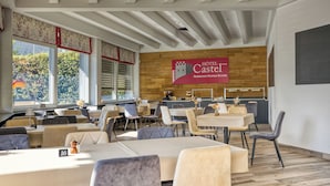 Un comedor de hotel con mesas y sillas, una pared de madera con un letrero y ventanas amplias.