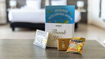 A hotel room with a bed, a thank you card, a coloring book, and a snack package.