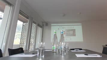 Ein Konferenzraum mit großem Tisch, Wasserflaschen, Gläsern und einer Projektionsleinwand, auf der ein Hotelname angezeigt wird.