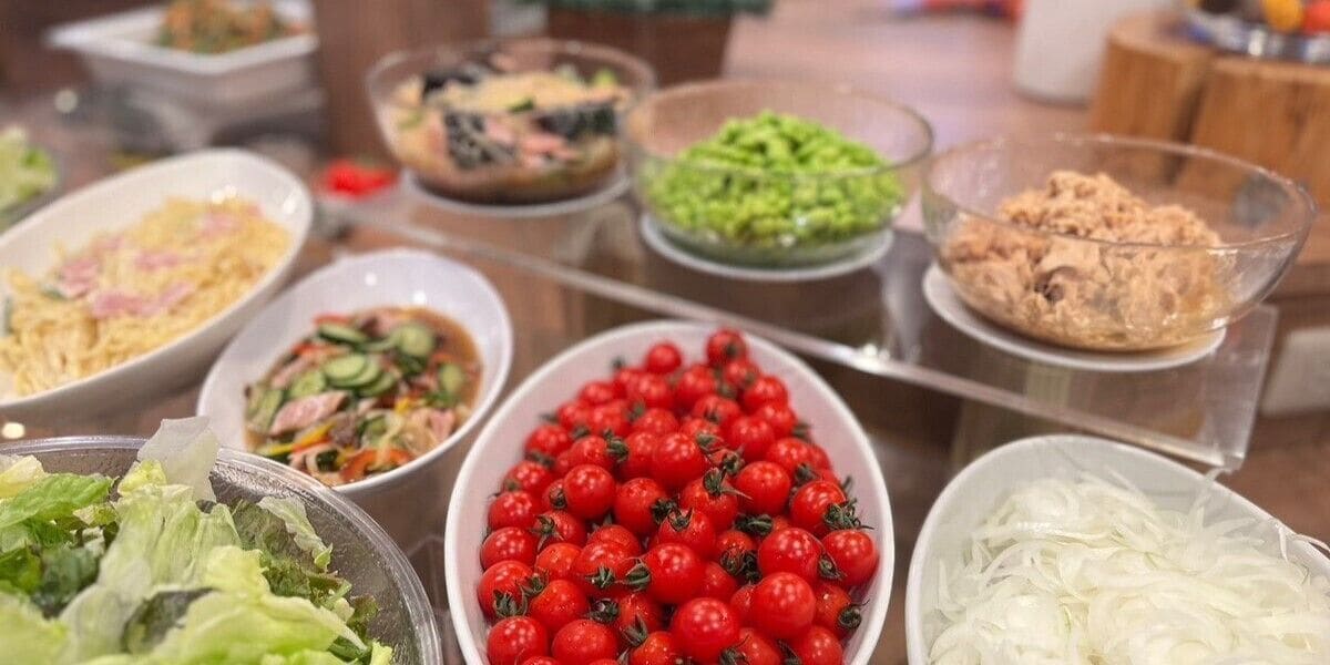 A buffet with various dishes including salads, a bowl of cherry tomatoes, and other prepared foods.