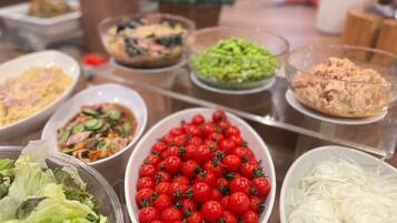 A buffet with various dishes including salads, a bowl of cherry tomatoes, and other prepared foods.