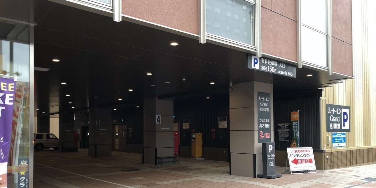 Entrada de un hotel con un letrero de estacionamiento, un letrero que dice Grand Hotel y un letrero de Honda.