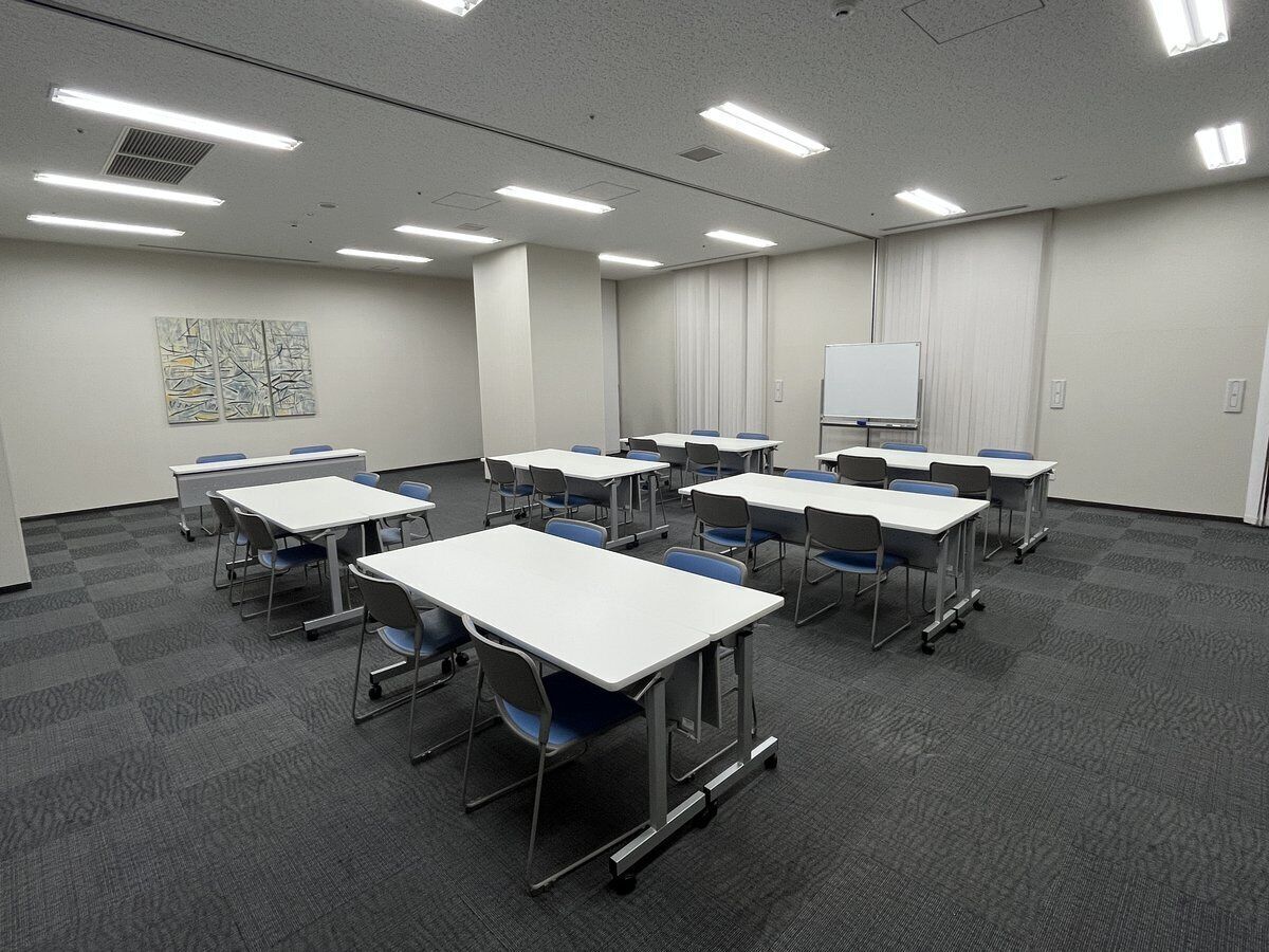 A conference room with multiple tables and chairs, a whiteboard, and a carpeted floor.