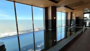 Un área de piscina interior moderna con amplios ventanales que ofrecen vista al mar y al paisaje urbano.