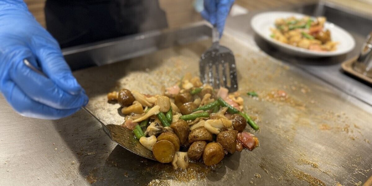 A person wearing blue gloves preparing food on a stainless steel surface.
