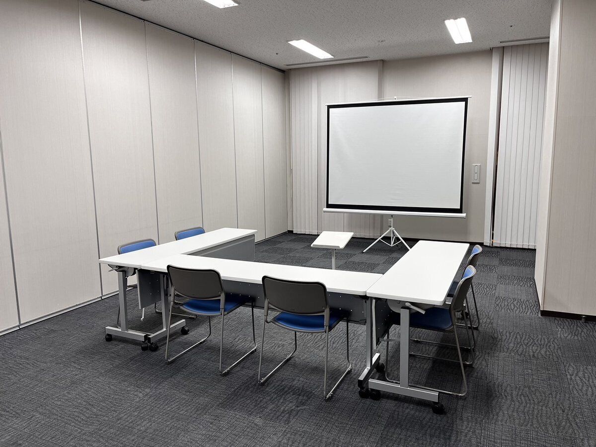 A conference room with a large table, four chairs, a projector screen, and a whiteboard.