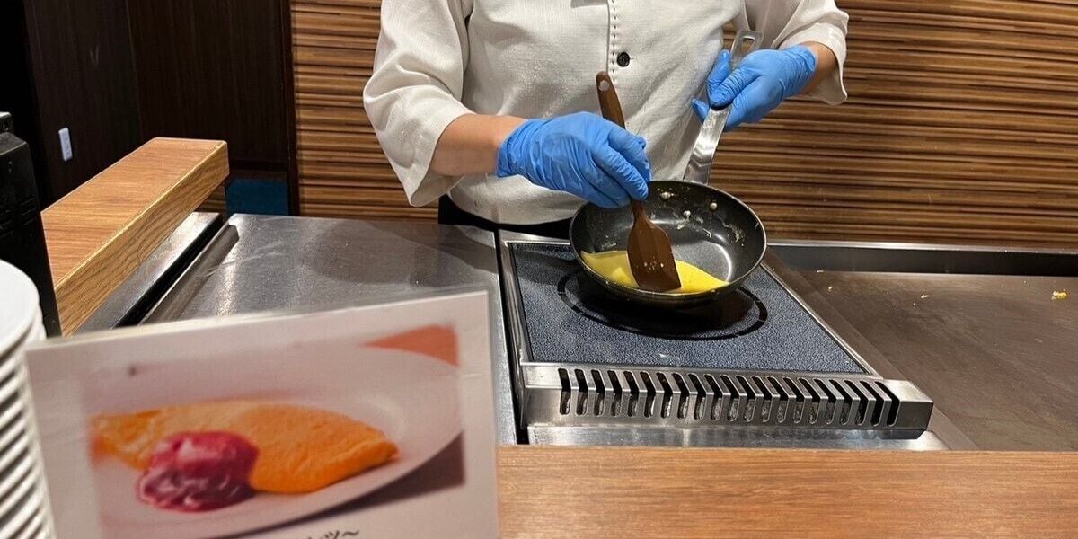 A person wearing a chef's uniform and blue gloves, cooking on a stovetop.