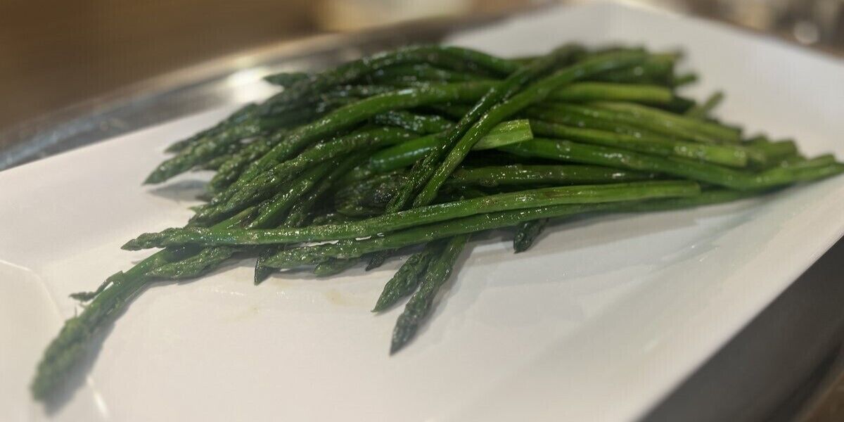 A white plate with cooked green asparagus.
