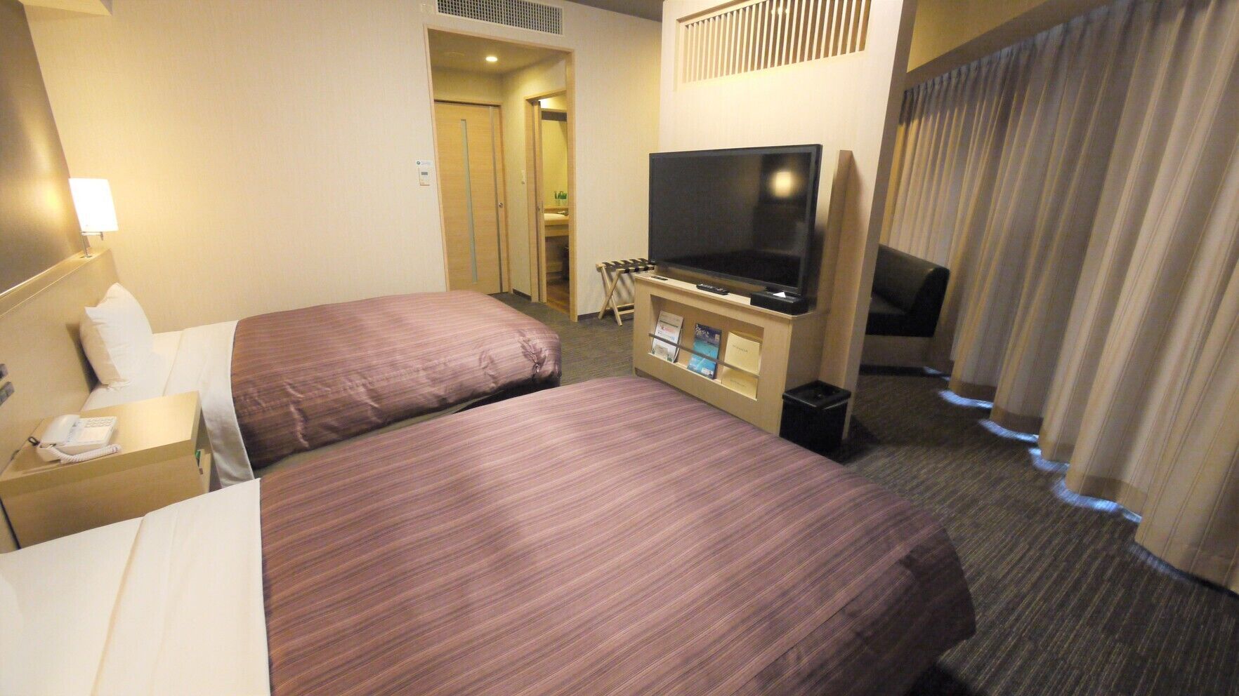 Ein Hotelzimmer mit zwei Betten, einem Fernseher, einem Schreibtisch mit Telefon und einem Papierkorb.