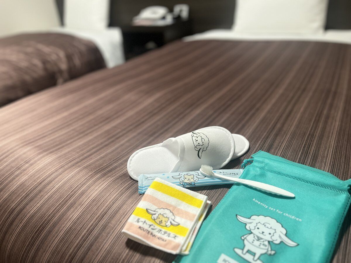 A bed with a brown striped cover, a white pillow with a sheep design, a toothbrush, a toothbrush holder, and a teal bag labeled "Amenity set for children".