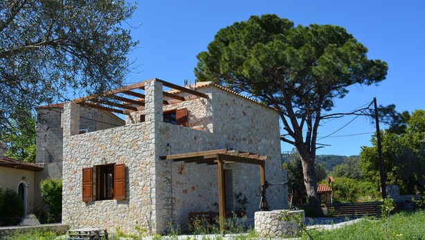 A stone building with a wooden pergola, surrounded by greenery and trees. - Pyrgos Luxury Country Home (Rhodes)