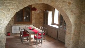 A stone-walled dining area with a table and chairs, a window, and a radiator. - Pyrgos Luxury Country Home (Rhodes)