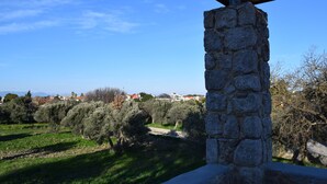 A stone pillar with a wooden beam above it, overlooking a green landscape with trees and a distant view of houses. - Pyrgos Luxury Country Home (Rhodes)